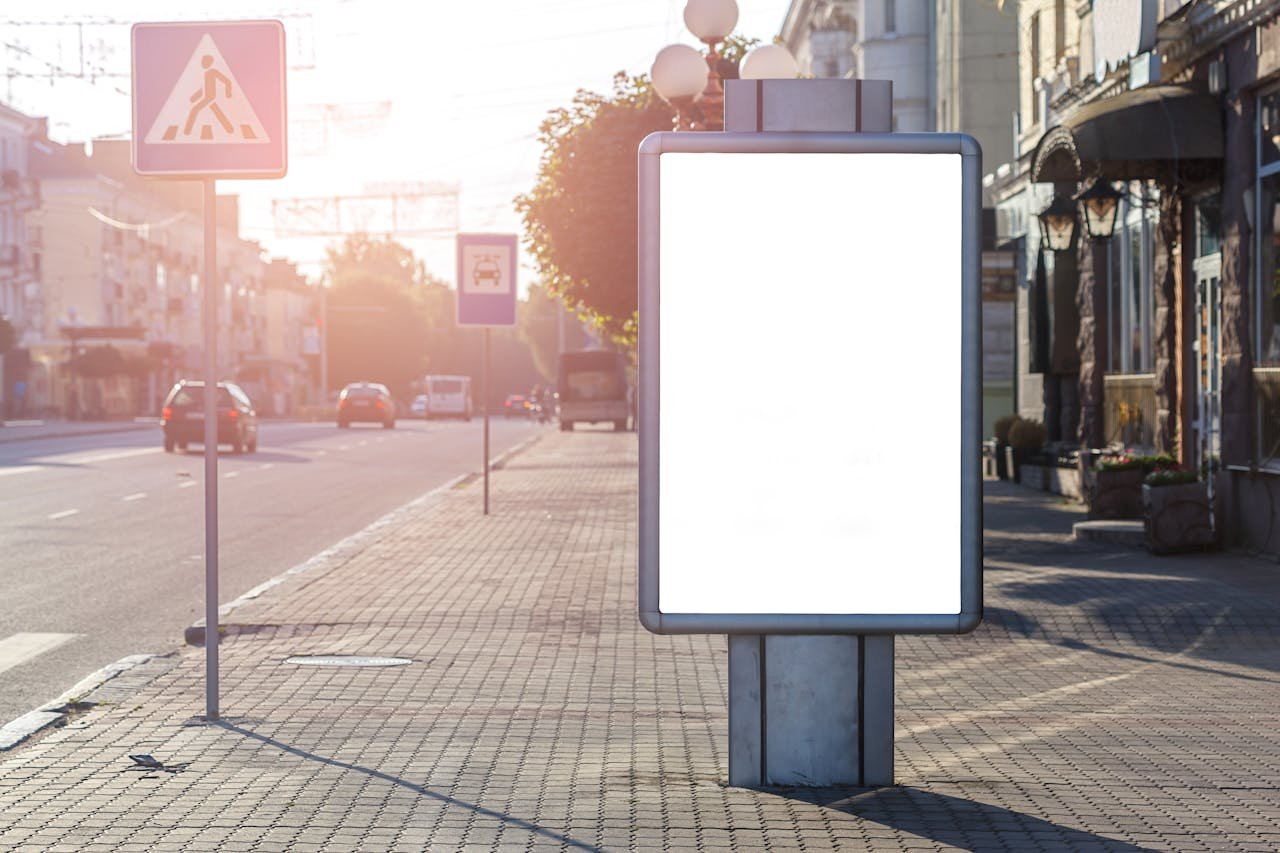 Blank advertisement on tiled walkway with road signs and building in town on sunny day